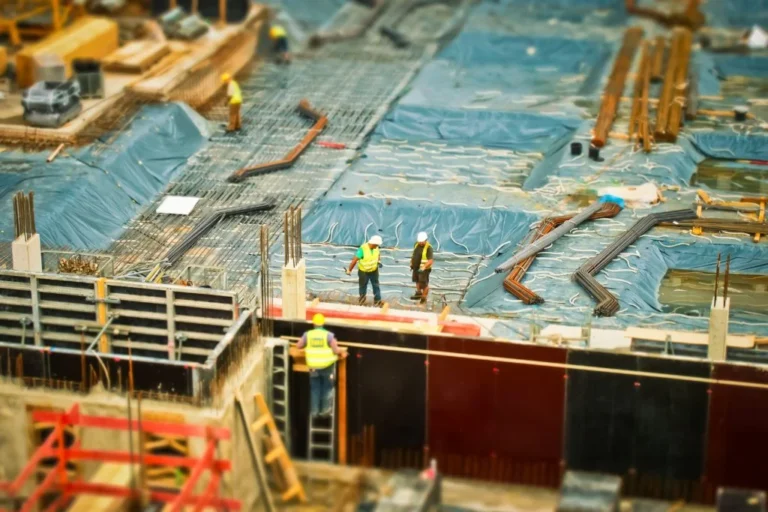 Construction site with workers, foundation work, rebar, equipment, and project materials